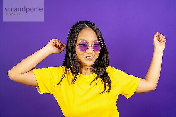 Studio Foto mit lila Hintergrund von einer chinesischen Frau mit Sonnenbrille tanzen und lächelnd