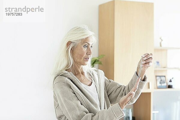 Ältere Frau mit langen Haaren schaut auf eine eine Halskette zu Hause
