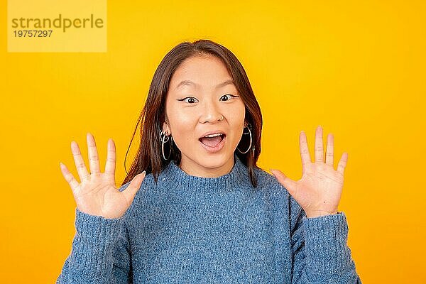 Studiofoto mit gelbem Hintergrund von einer überraschten chinesischen jungen Frau  die in die Kamera schaut