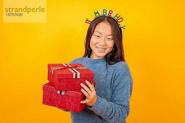 Studiofoto mit gelbem Hintergrund von einer chinesischen Frau  die Geschenke für ihren Geburtstag erhält