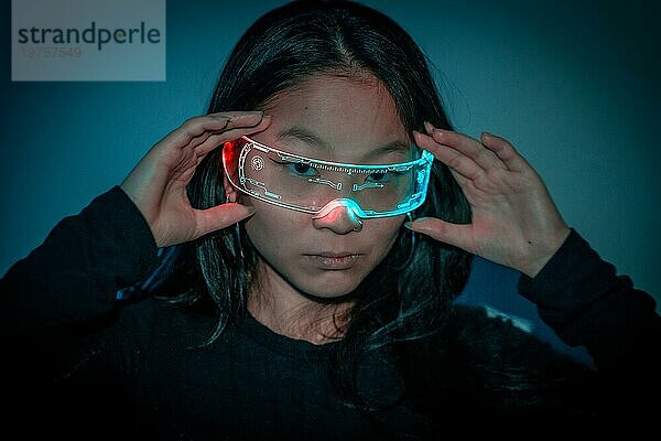 Studiofoto mit blauem Hintergrund mit Neonlicht von einer chinesischen Frau mit kybernetischer Brille  die in die Kamera schaut