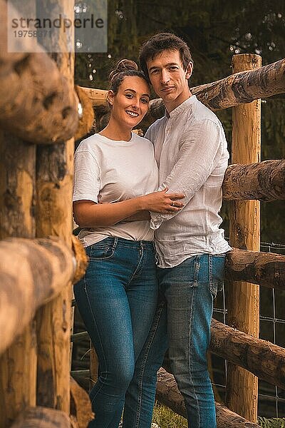 Vertikales Porträt eines Paares  das zwischen Holzschienen in einem Park lächelnd in die Kamera schaut