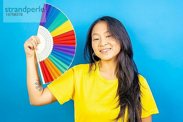 Studiofoto mit blauem Hintergrund einer chinesischen Frau  die einen regenbogenfarbenen Fächer benutzt