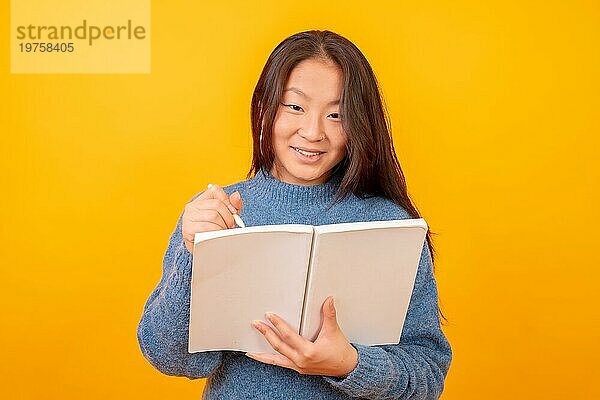 Studiofoto mit gelbem Hintergrund einer chinesischen Frau  die ein Notizbuch hält und studiert