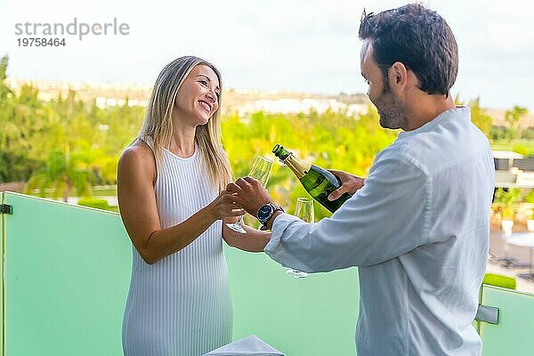 Mann serviert seiner Partnerin Champagner auf der Terrasse eines Luxushotels