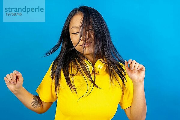 Studio Foto mit blauem Hintergrund einer chinesischen Frau mit Kopfhörern tanzen freestyle