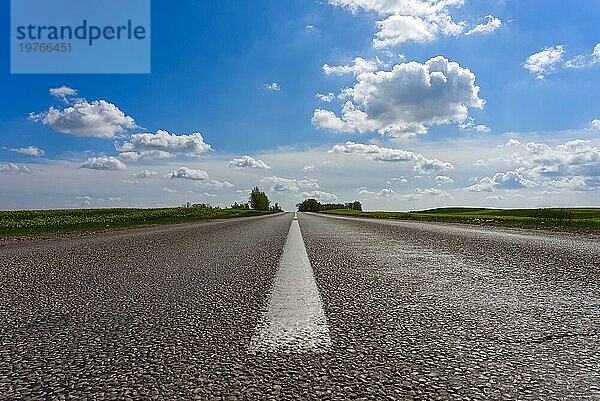 Niedriger Blickwinkel auf eine geteerte Straße  die in der Ferne in offener Landschaft unter einem bewölkten blaün Himmel verschwindet  mit Fokus auf die mittlere weiße Linie