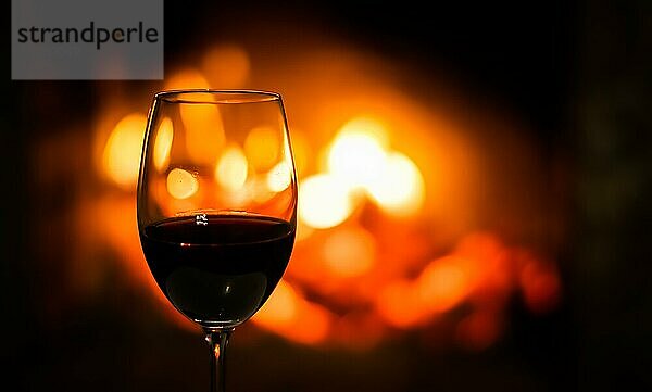 Ein Weinglas mit Rotwein auf dem Hintergrund der Kaminbeleuchtung. Weihnachten Urlaub Konzept