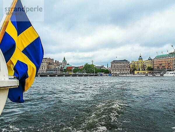 Panoramablick vom Ausflugsboot mit der schwedischen Flagge auf die schönen Gebäude von Stromkajen im Zentrum von Stockholm Schweden