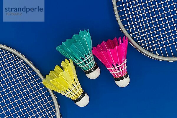 Badminton. Schläger und bunte gefiederte Federbälle in blau  gelb und rosa auf blauem Hintergrund in Draufsicht mit freiem Kopierraum