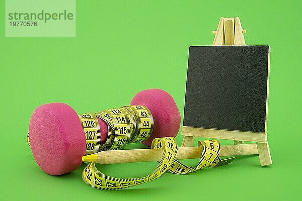 Start gesunder Lebensstil Konzept. Stillleben mit rosa Hantel  Maßband  Kreidetafel und Bleistift auf grünem Hintergrund