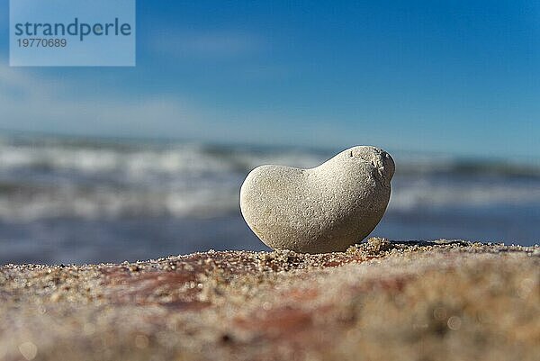Heart shaped waterborne smooth rock balanced at the beach overlooking the waves and sea with selective focus conceptual of summer holidays at the coast