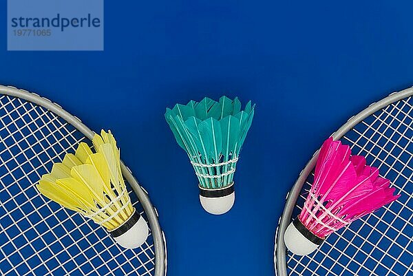 Badminton. Schläger und bunte gefiederte Federbälle in blau  gelb und rosa auf blauem Hintergrund in Draufsicht mit freiem Kopierraum