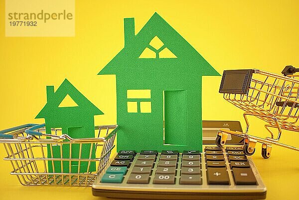 Kaufen Sie eine größere oder kleinere Häuser Konzept mit zwei verschiedenen Größen von Häusern  Warenkorb und Rechner auf gelbem Hintergrund