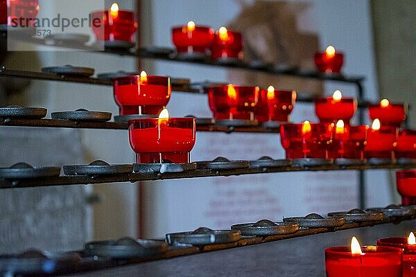 Brennende rote Gebetskerzen in einer katholischen Kirche auf einem Kerzenständer. Selektiver Fokus