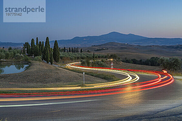 Blick auf Autospurlichter in der toskanischen Landschaft in der Nähe von Pienza in der Abenddämmerung  Pienza  Provinz Siena  Toskana  Italien  Europa