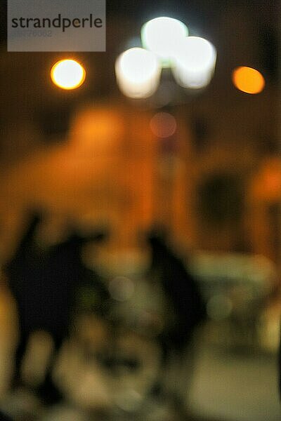 Straßenszene  Placa  Plaça de la Vila de Gràcia  Passanten  Silhouetten vor beleuchteter Hausfassade in der Nacht  Bokeh  Textur  Illustration  Symbolbild  Nachtleben  Szeneviertel  Stadtteil Gracia  Barcelona  Spanien  Europa