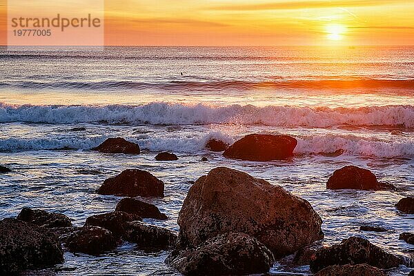 Sonnenuntergang über dem Atlantik mit Wellen und Felsen und Surfer Silhouetten im Wasser an der Costa da Caparica  Portugal  Europa