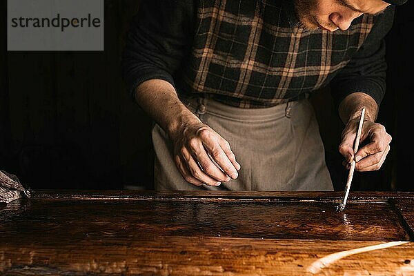 Handwerker lackiert eine Holzplatte eines Schrankes aus Massivholz. Arbeit in der Werkstatt Restaurierung