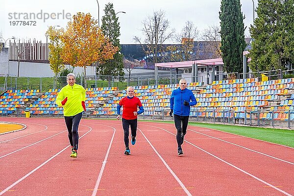 Frontalansicht von drei reifen  sportlichen Männern  die auf einer Leichtathletikbahn laufen