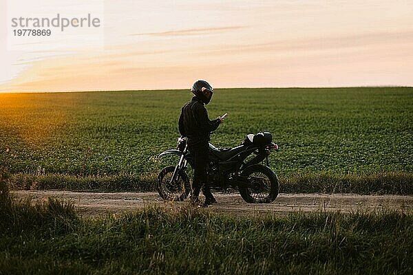 Männlicher Motorradfahrer auf einer Landstraße mit einer Enduro bei Sonnenuntergang