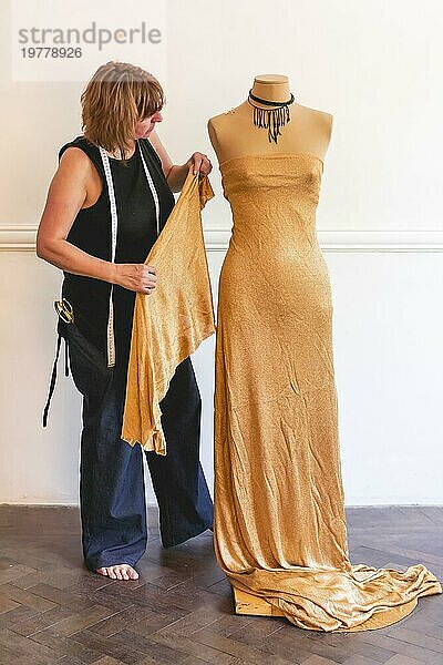 Modedesignerin bei der Arbeit an einem Kleidungsstück und einem Kleid  das über einer Schaufensterpuppe hängt
