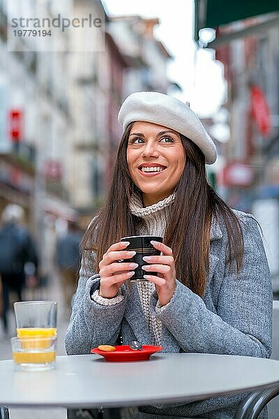 Vertikales Foto einer eleganten Frau  die an einem kalten Tag in einer Cafeteria im Freien heißen Kaffee trinkt
