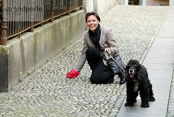 Glückliche Frau mit ihrem niedlichen Hund Reinigung der Straße von Hundekot in der Schweiz