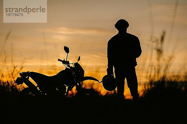 Silhouette eines Motorrads und eines Motorradfahrers bei Sonnenuntergang auf einem Feld  Enduro Geländemotorrad