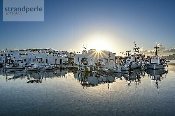 Fischerboote im Hafen von Naoussa bei Sonnenuntergang  spiegeln sich im Meer  Sonnenstern  Weiße kykladische Häuser  Naoussa  Paros  Kykladen  Griechenland  Europa