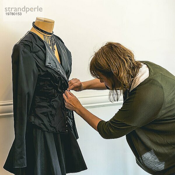 Modedesigner  der eine Schaufensterpuppe mit schwarzer Kleidung anzieht