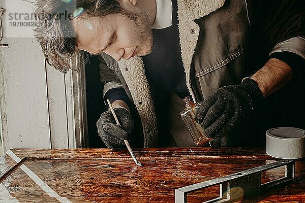 Handwerker lackiert eine Holzplatte eines Schrankes aus Massivholz. Arbeit in der Werkstatt Restaurierung