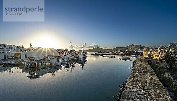 Fischerboote im Hafen von Naoussa bei Sonnenuntergang  spiegeln sich im Meer  Sonnenstern  rechts Ruinen der venezianischen Burg  weiße kykladische Häuser  Naoussa  Paros  Kykladen  Griechenland  Europa