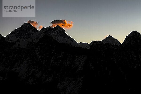 Blick in Richtung Osten bei Tagesanbruch vom Gokyo Ri  dem beliebten Trekking Gipfel und Aussichtspunkt in der Everest Region. Die Silhouetten von drei Achttausendern sind zu sehen  die von der aufgehenden Sonne angestrahlt werden: Der Mount Everest befindet sich unter der orangefarbenen Wolke auf der linken Seite  dann folgt der Lhotse  der vierthöchste Berg der Erde. Der Makalu mit seiner pyramidenartigen Form ist weiter rechts zu sehen. Gokyo Trek  Khumbu  Everest Region  Himalaya. Der Sagarmatha Nationalpark  ein UNESCO Welterbe. Solukhumbu  Nepal  Asien