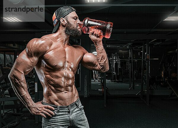 Muskulöser Mann im Fitnessstudio trinkt aus einer großen Flasche. Fitness und Bodybuilding Konzept. Gemischte Medien