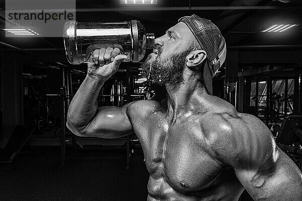 Muskulöser Mann im Fitnessstudio trinkt aus einer großen Flasche. Fitness und Bodybuilding Konzept. Gemischte Medien