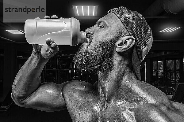 Muskulöser Mann im Fitnessstudio trinkt aus einem Shaker. Fitness und Bodybuilding Konzept. Gemischte Medien