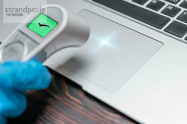 Bild einer Hand in einem medizinischen Handschuh  die die Temperatur eines Laptops misst. Konzept für Antivirensysteme. Schutz des Computers vor Hackerangriffen. Erfolgreiches Ergebnis. Gemischte Medien