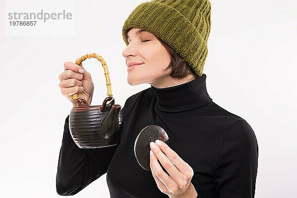 Porträt einer lächelnden Frau mit grüner Strickmütze  die das Aroma von Kräutertee genießt. Teezeremonie. Gemischte Medien