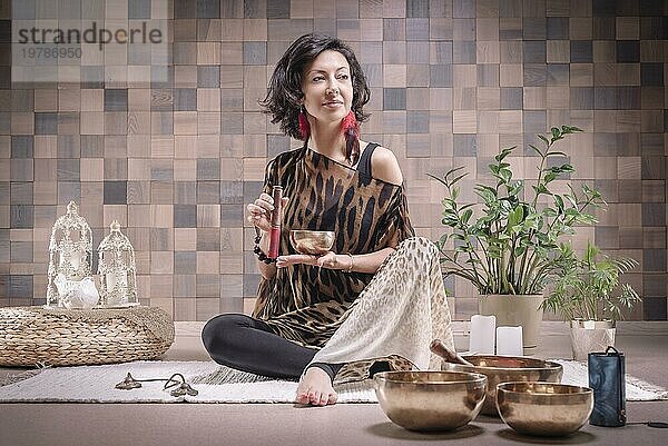 Bild einer erwachsenen Frau im Yogaraum. Spielen auf tibetischen Klangschalen. Das Konzept von Yoga und spirituellen Praktiken. Gemischte Medien