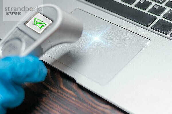 Bild einer Hand in einem medizinischen Handschuh  die die Temperatur eines Laptops misst. Konzept für Antivirensysteme. Schutz des Computers vor Hackerangriffen. Erfolgreiches Ergebnis. Gemischte Medien