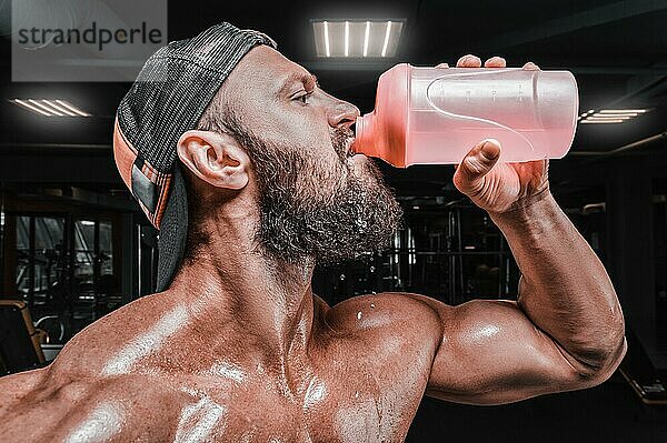 Muskulöser Mann im Fitnessstudio trinkt aus einem Shaker. Fitness und Bodybuilding Konzept. Gemischte Medien