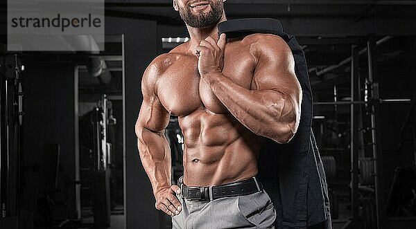 Attraktiver Mann in grauer Hose posiert in der Turnhalle. Business und Bodybuilding Konzept. Sportliche Aktivitäten. Gemischte Medien