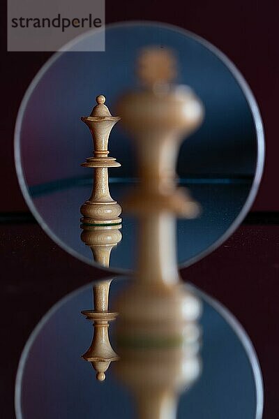 Eine Dame-Schachfigur ist in einem Spiegel zu sehen  davor steht ein König auf sich spiegelndem Untergrund  Schachspiel  Symbolbild für Macht  Beziehung  Konflikt