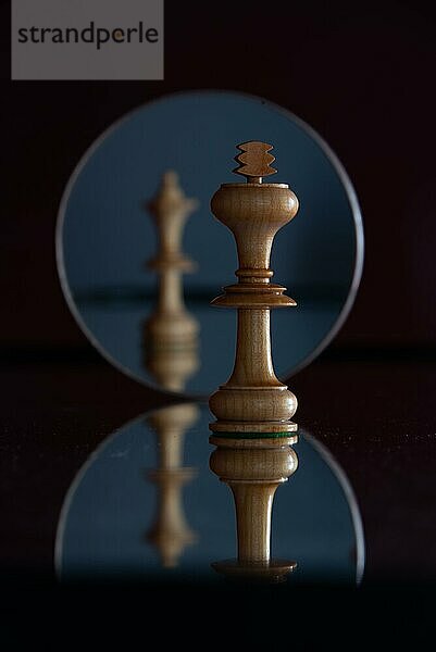 Spiegelung einer Dame-Schachfigur in einem Spiegel  davor mit scharfem Fokus eine König-Schachfigur  Schachfiguren  Symbolbild für Macht  Beziehung  Konflikte