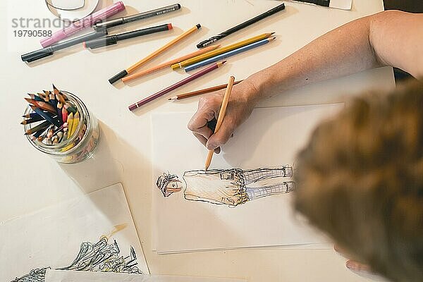 Draufsicht auf einen Modedesigner  der eine Modeskizze mit bunten Bleistiften zeichnet
