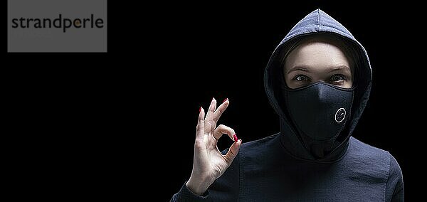 Porträt eines Mädchens mit Schutzmaske  das einen Daumen nach oben zeigt. Das Konzept des Kampfes gegen die Epidemie. Gemischte Medien