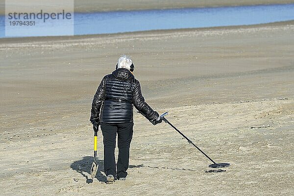 Ältere Frau mit Metalldetektor beim Strandspaziergang am Sandstrand an der Nordseeküste im Winter