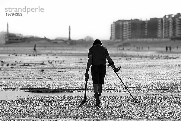 Mann mit Metalldetektor bei einer Strandbegehung am Sandstrand an der Nordseeküste an einem frühen Morgen im Sommer während der Ferienzeit