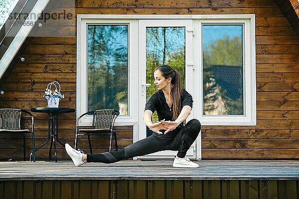 Aktive erwachsene Frau  die ihre Arme und Beine auf der Terrasse ihres Blockhauses ausstreckt